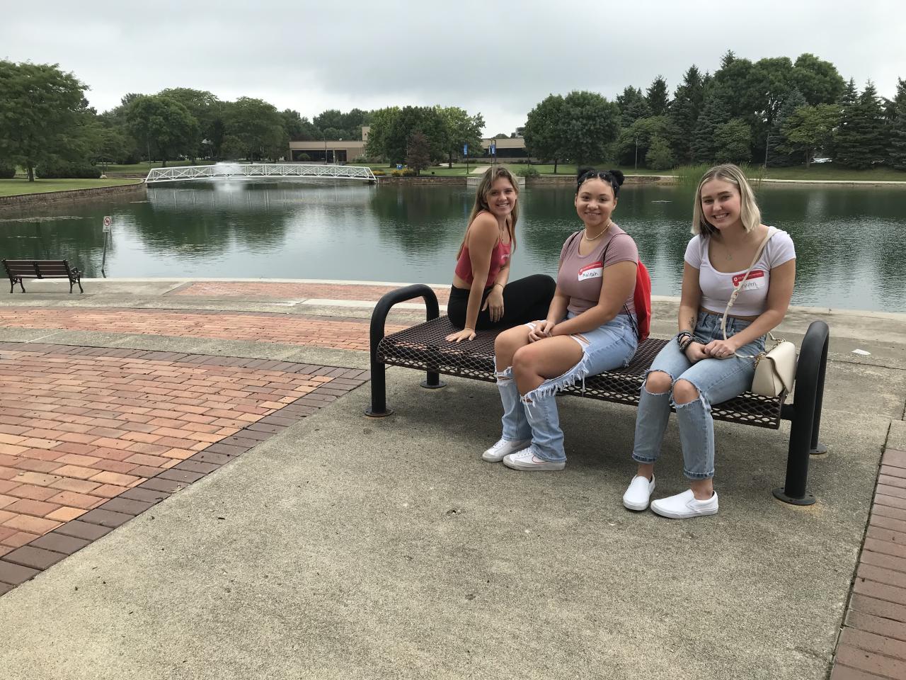 three young women on bench with pond in background