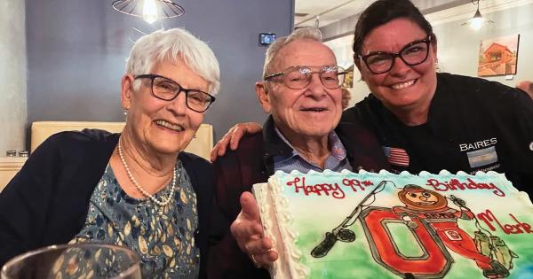 Older man in glasses with birthday cake surrounded by two smiling women