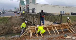 five people building a bridge connecting the existing 1.1 completed miles of the Marion Campus Trail near the north east corner of Bryson Hall to the Forum Shopping Center