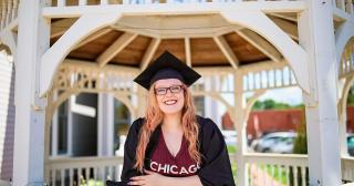 Red haired women with glasses, wearing a grad cap and gown stands in gazebo