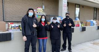 Group of 4 dressed in black stand in front of loading dock of food with thumbs up