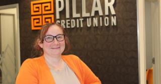 Woman in orange sweater and glasses in front of bank logo
