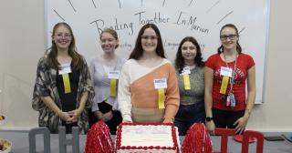 5 college students standing behind a cake