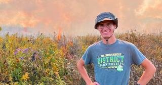 Young man in hat standing with prairie fire in the foreground