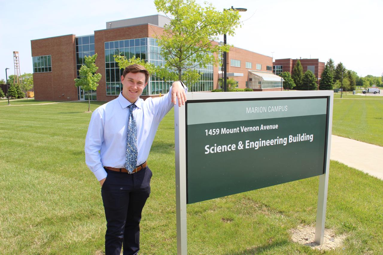 Young man in shirt and tie leaning on science building sign