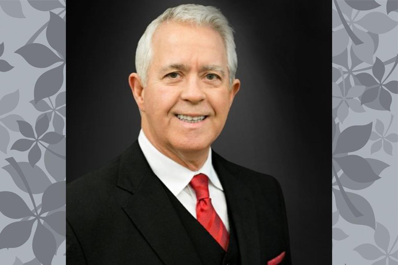 man grey hair black suit red tie leaf background