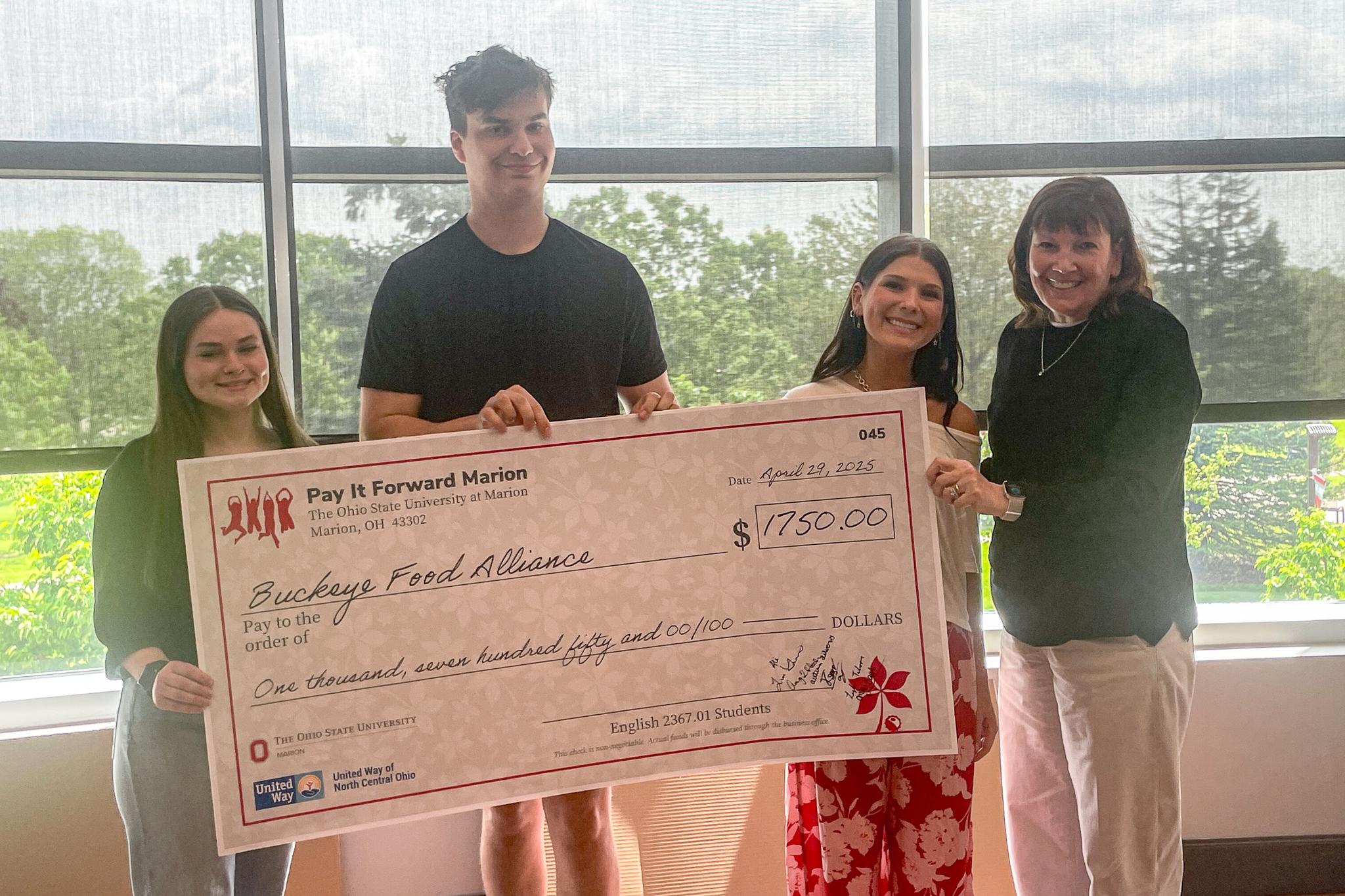 group of 4 holding large check in front of windows