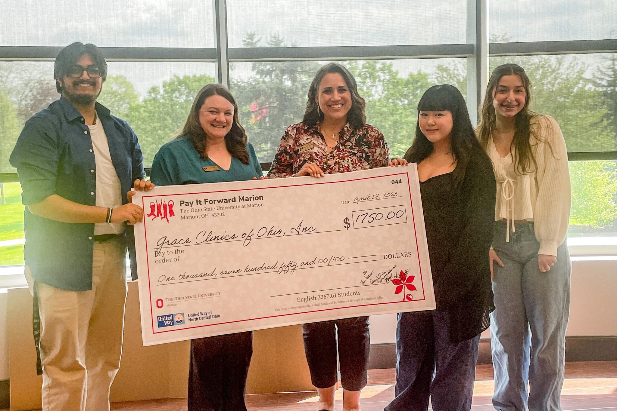 Group of five holding large check in front of windows