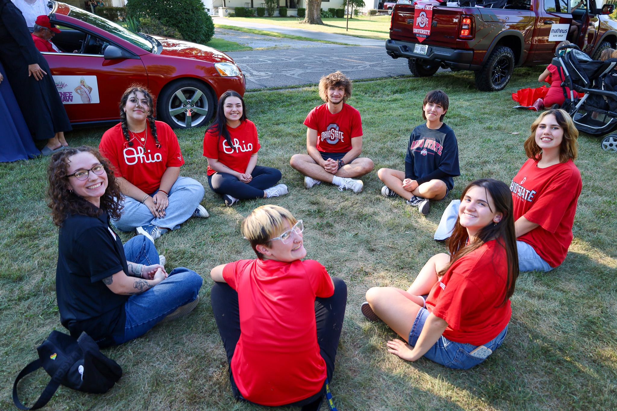 group of students in red seated in a circle on grass