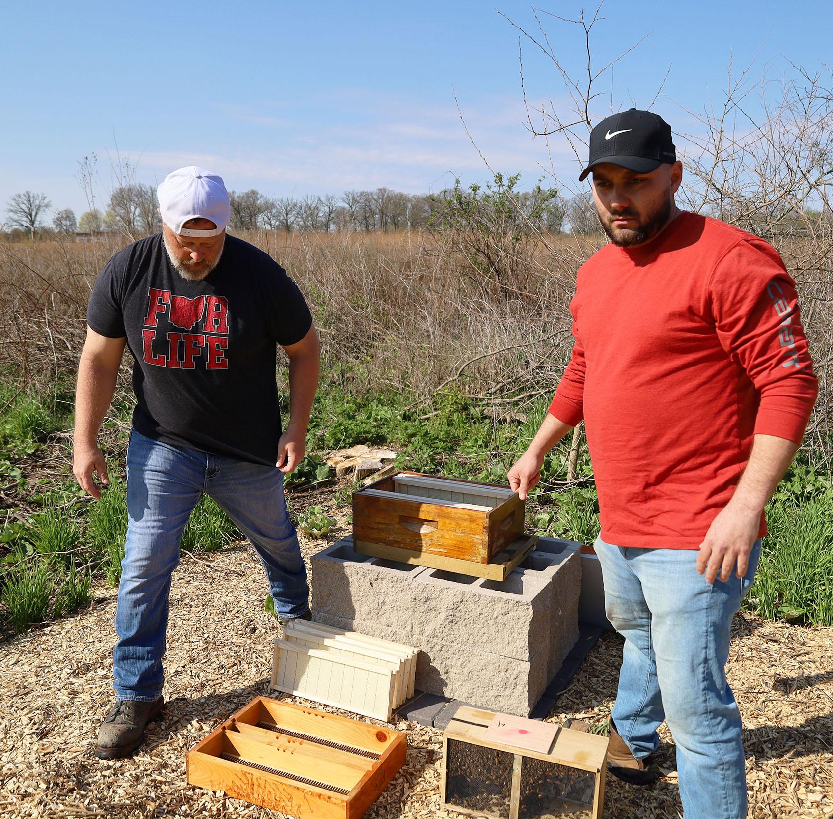 Two men in field with bee boxes