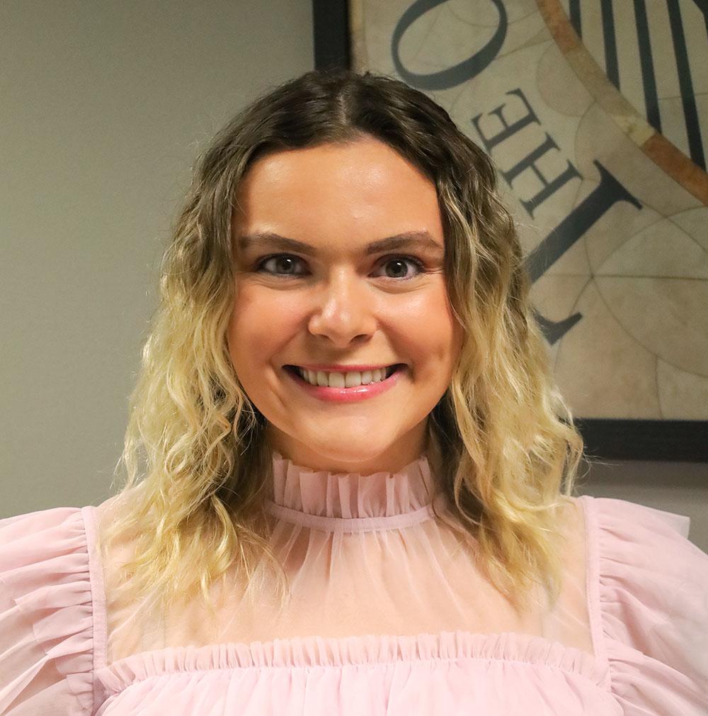 woman in pink blouse smiling in front of grey wall and picture