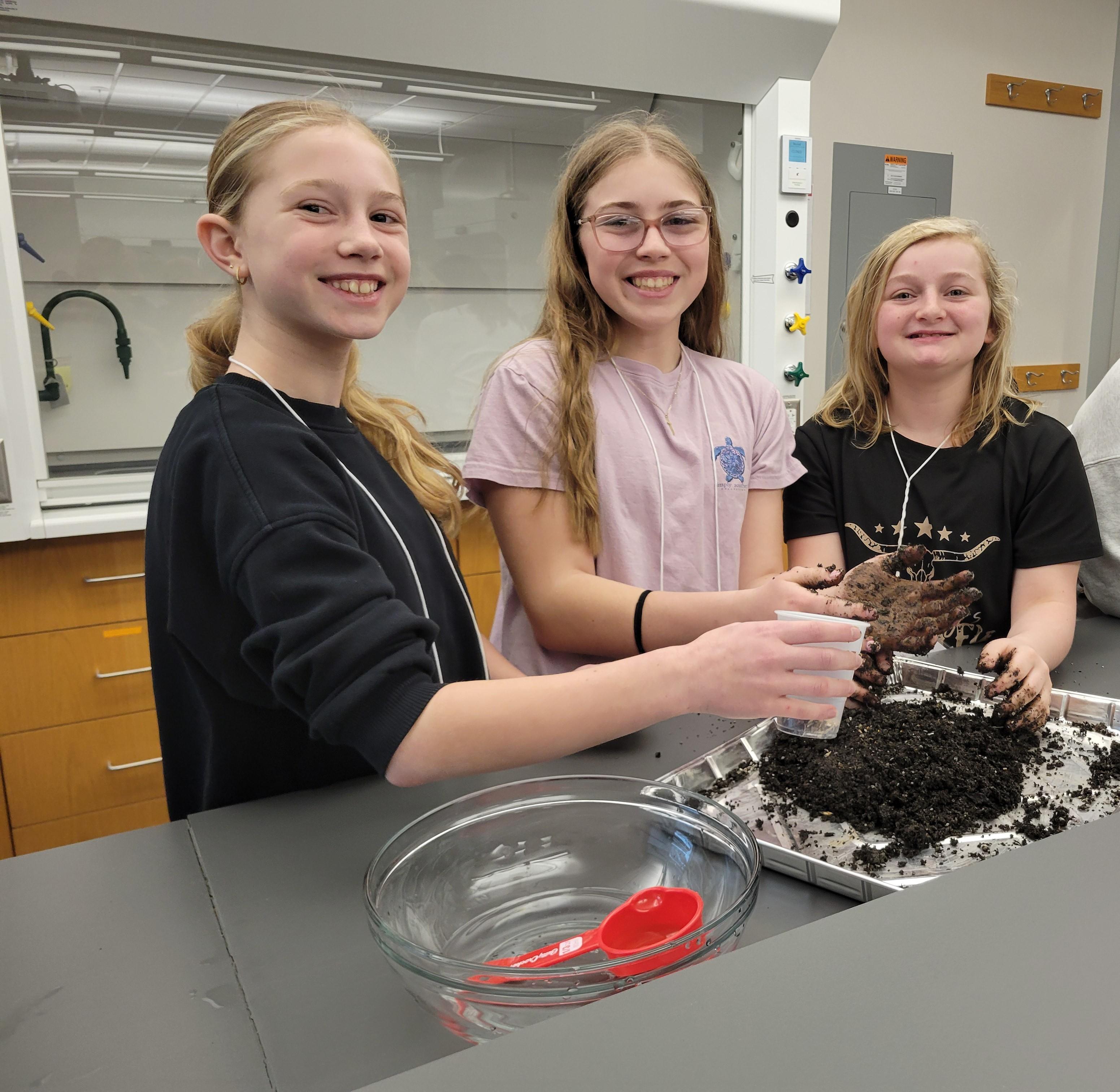 3 young girls hands in dirt in a lab