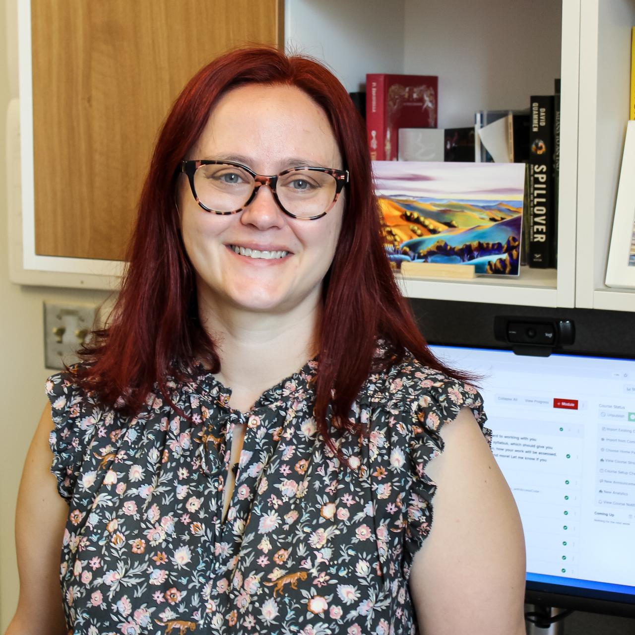 Woman with red hair and glasses in office smiling