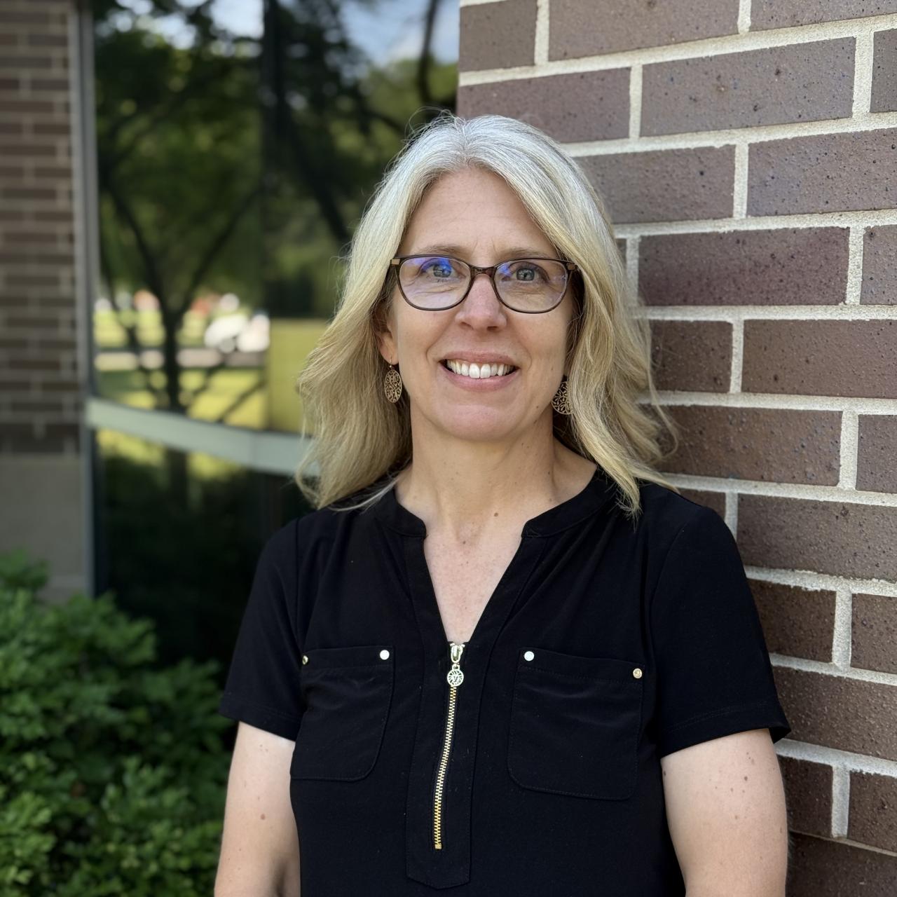 women in black shirt and glasses in front of brick building