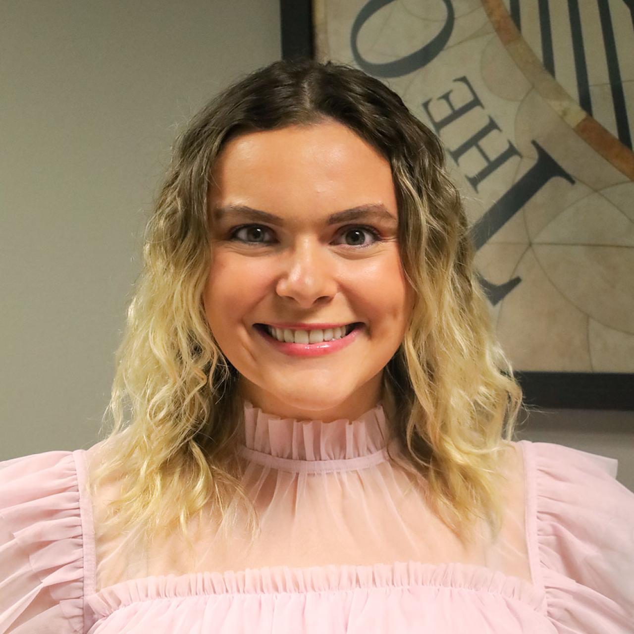 woman in pink blouse smiling in front of grey wall and picture