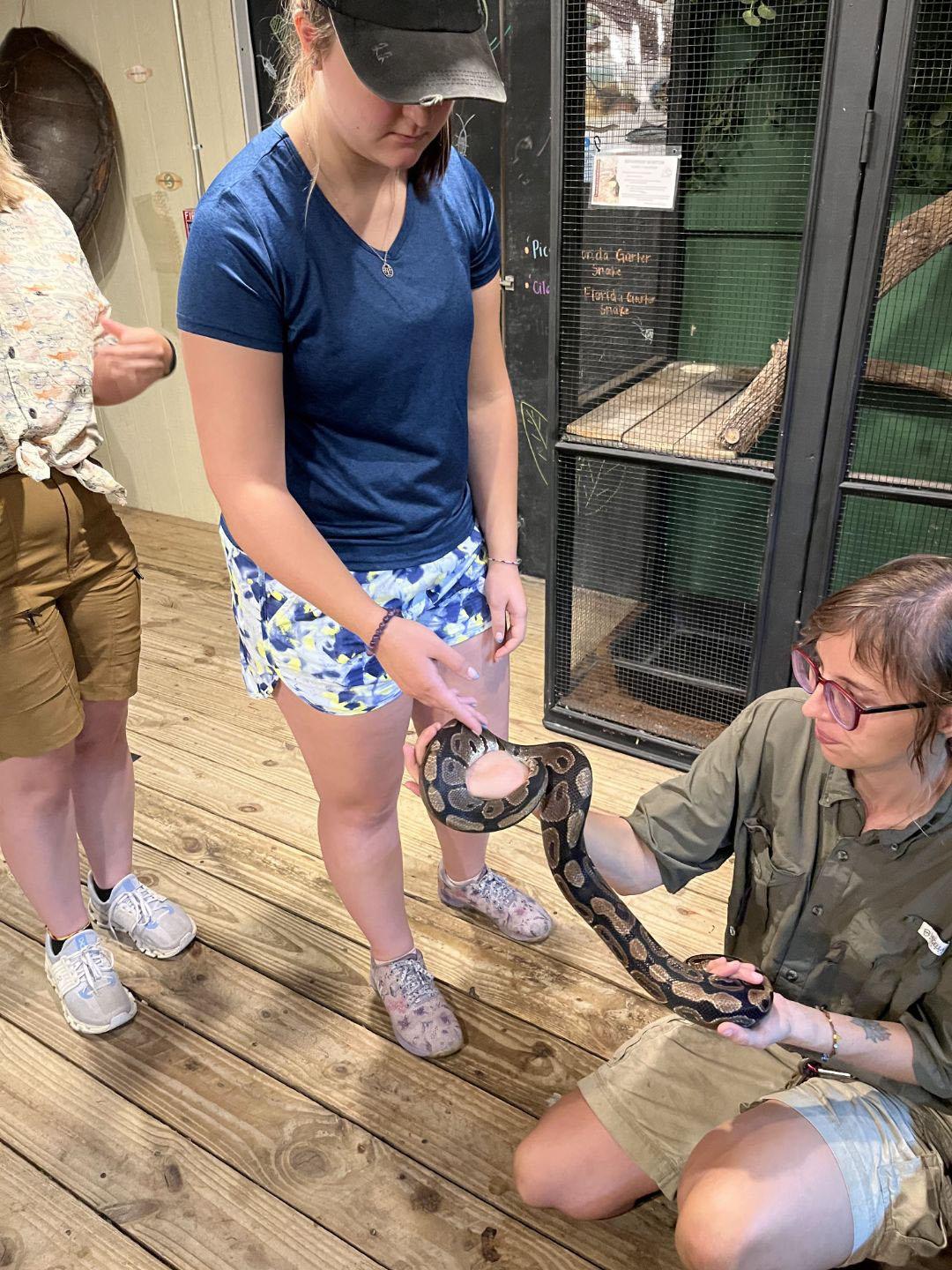 woman in ball cap observing snake being held by another woman