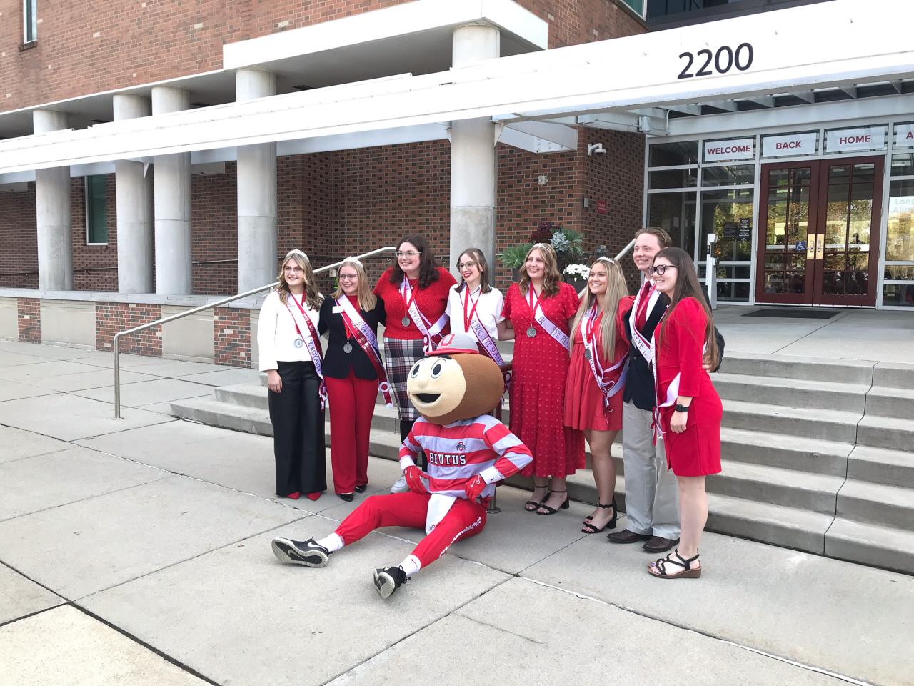 smaller group outside building steps with mascot