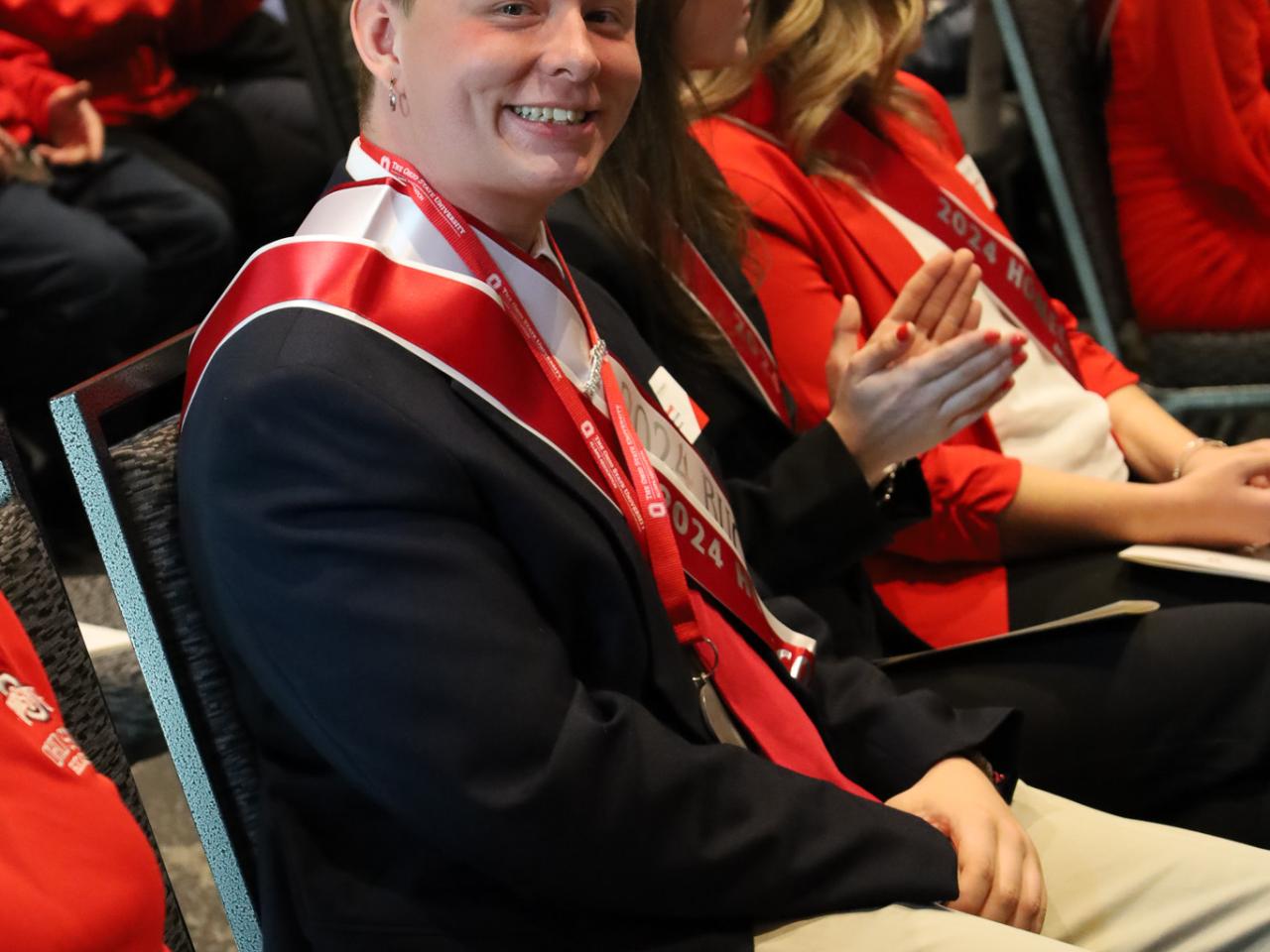 man in suit and sash looks left and smiles