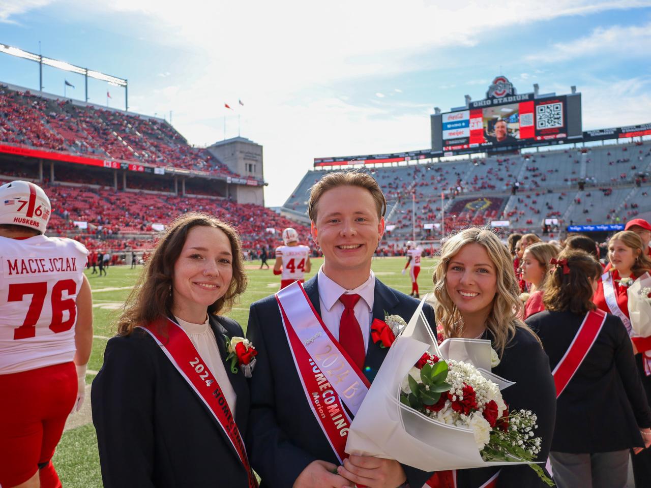 three students in suits inside football stadium on a sunny autumn day