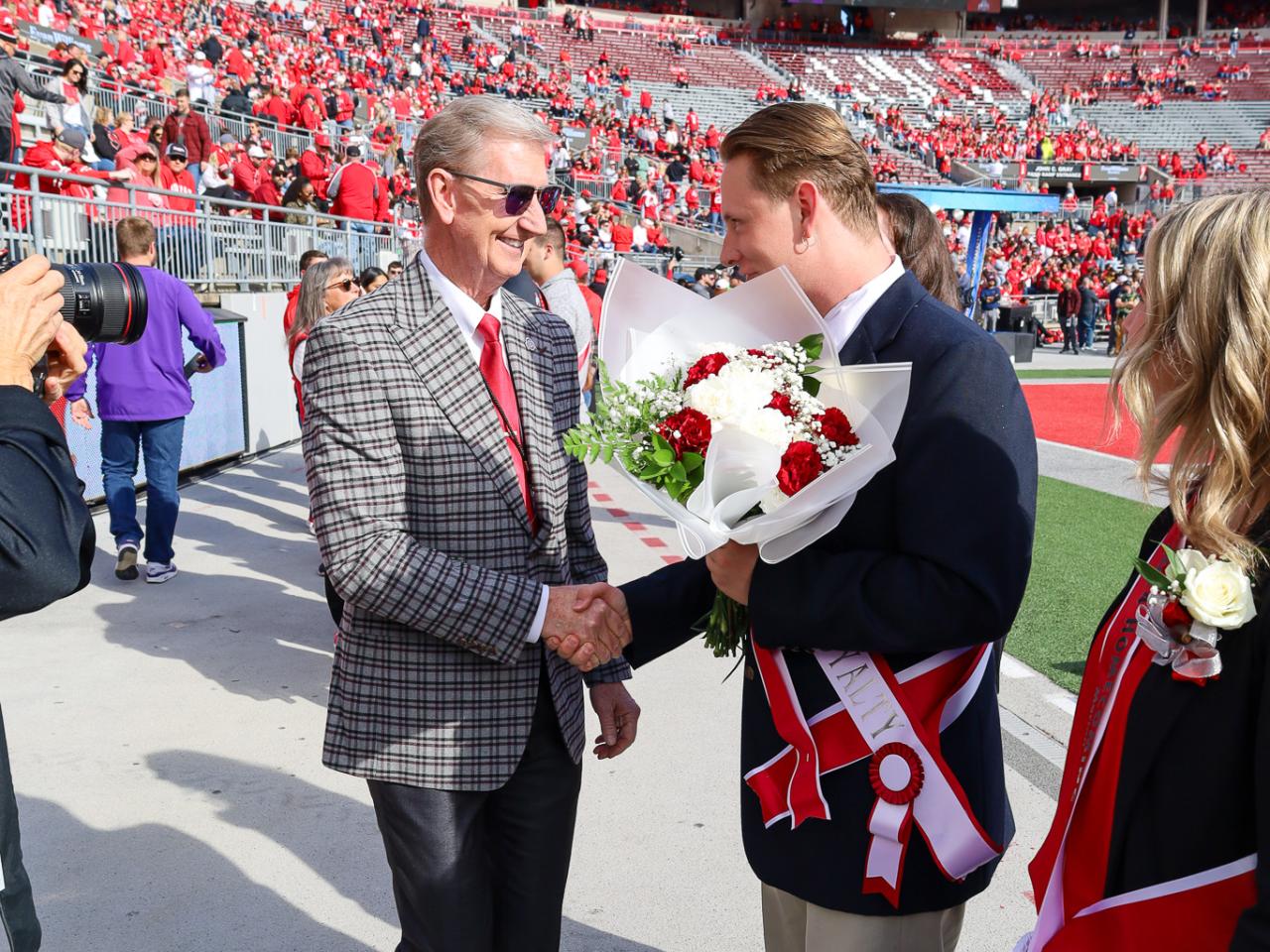 two men shaking hands on the sidelines of stadium