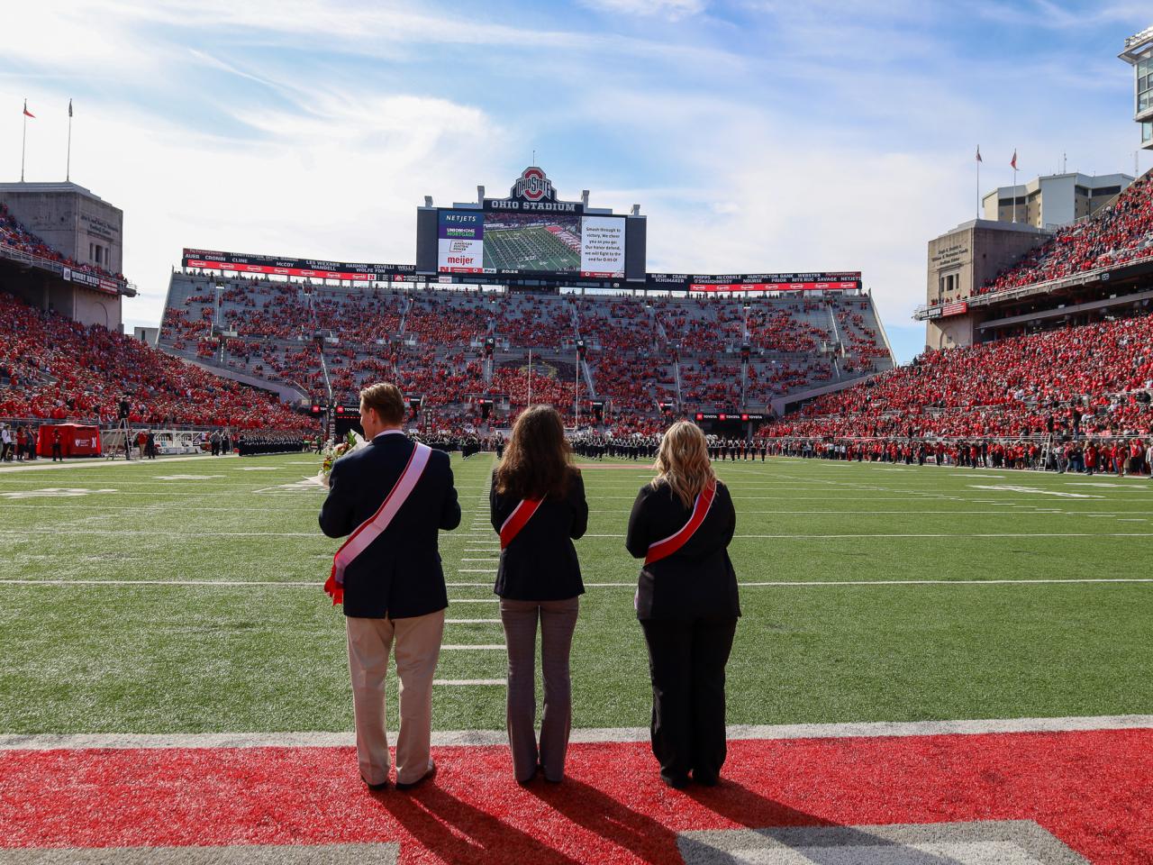 three in suits standing in stadium endzone looking down the field