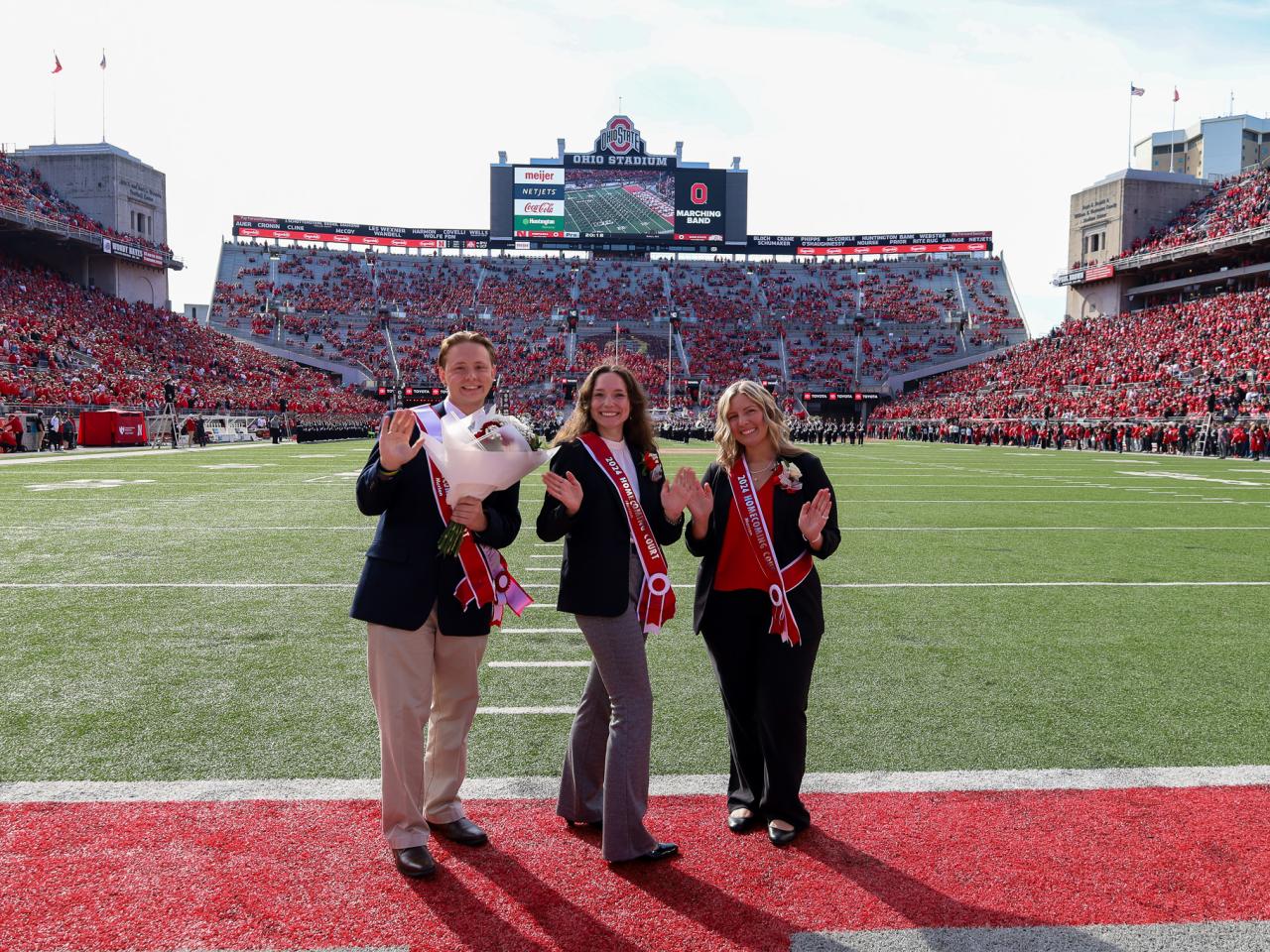 three in suits standing in stadium endzone turning to wave