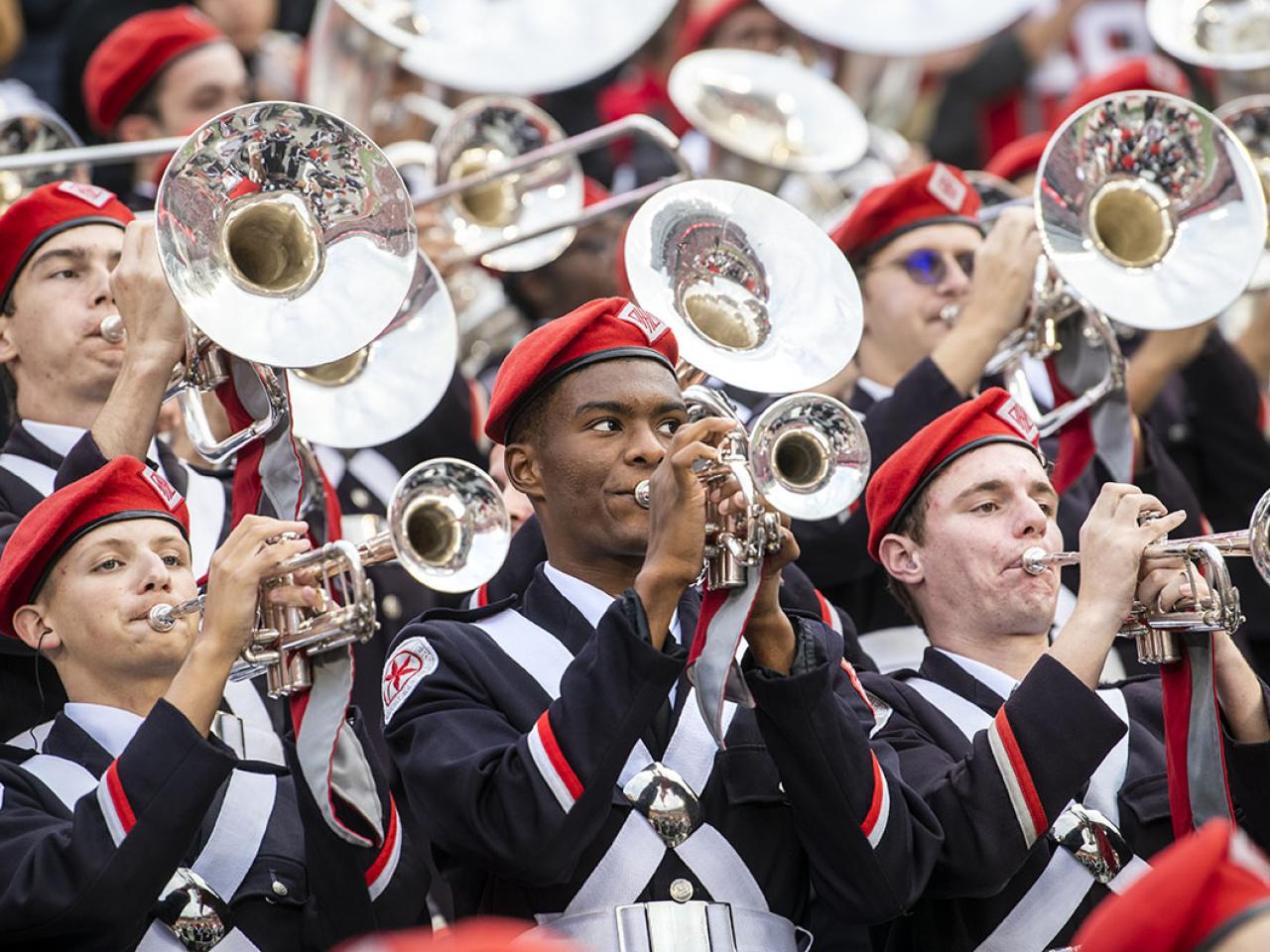 marching band group with silver brass instruments, black uniforms, and red beanies performing