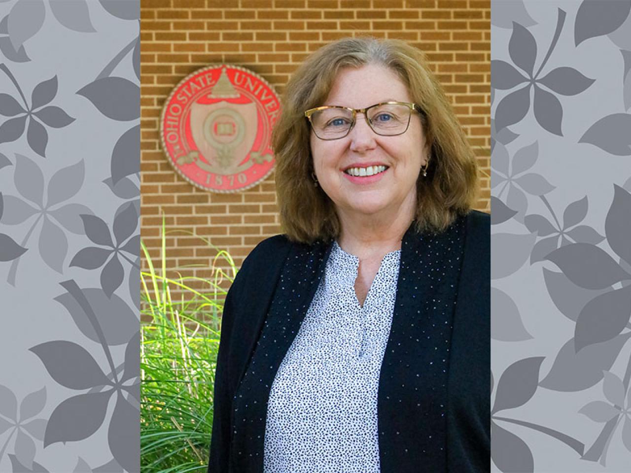 leaf background - woman in glasses and sports coat set against brick wall and university seal