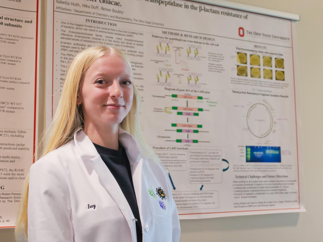 blonde woman in lab coat in front or cancer research poster