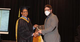 Man accepts academic award and shakes hand with man in academic regalia