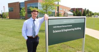Young man in shirt and tie leaning on science building sign