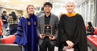 young man holding up plaque between college faculty in regalia