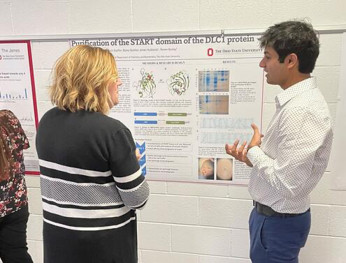 a student discusses his research poster with a staff member