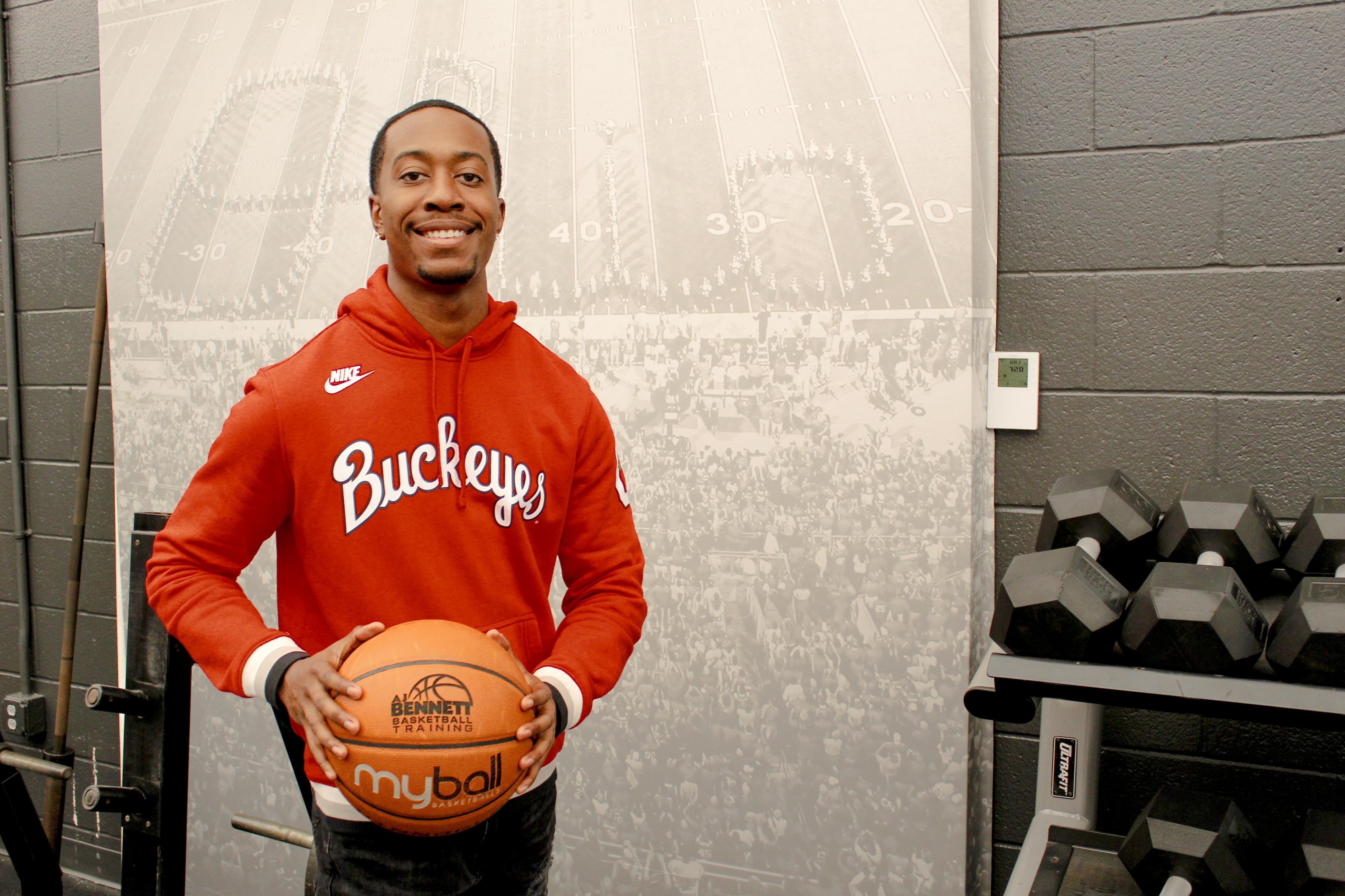 Man in red hoodie and basketball smiling in fitness center