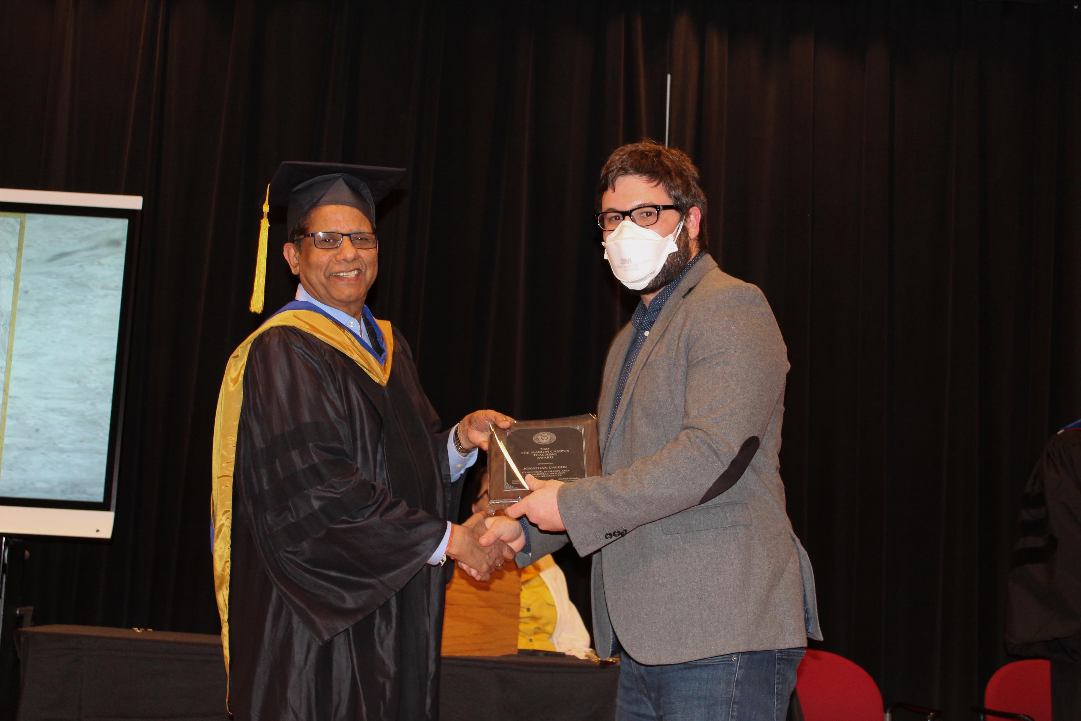 Man accepts academic award and shakes hand with man in academic regalia