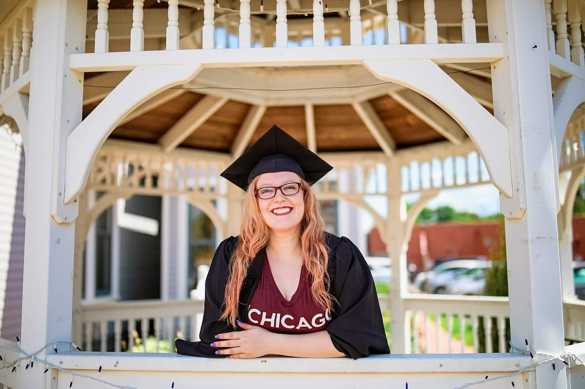 Red haired women with glasses, wearing a grad cap and gown stands in gazebo