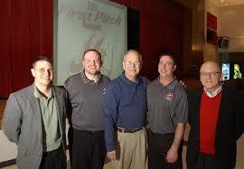Five men smiling in front of a first pitch banquet banner