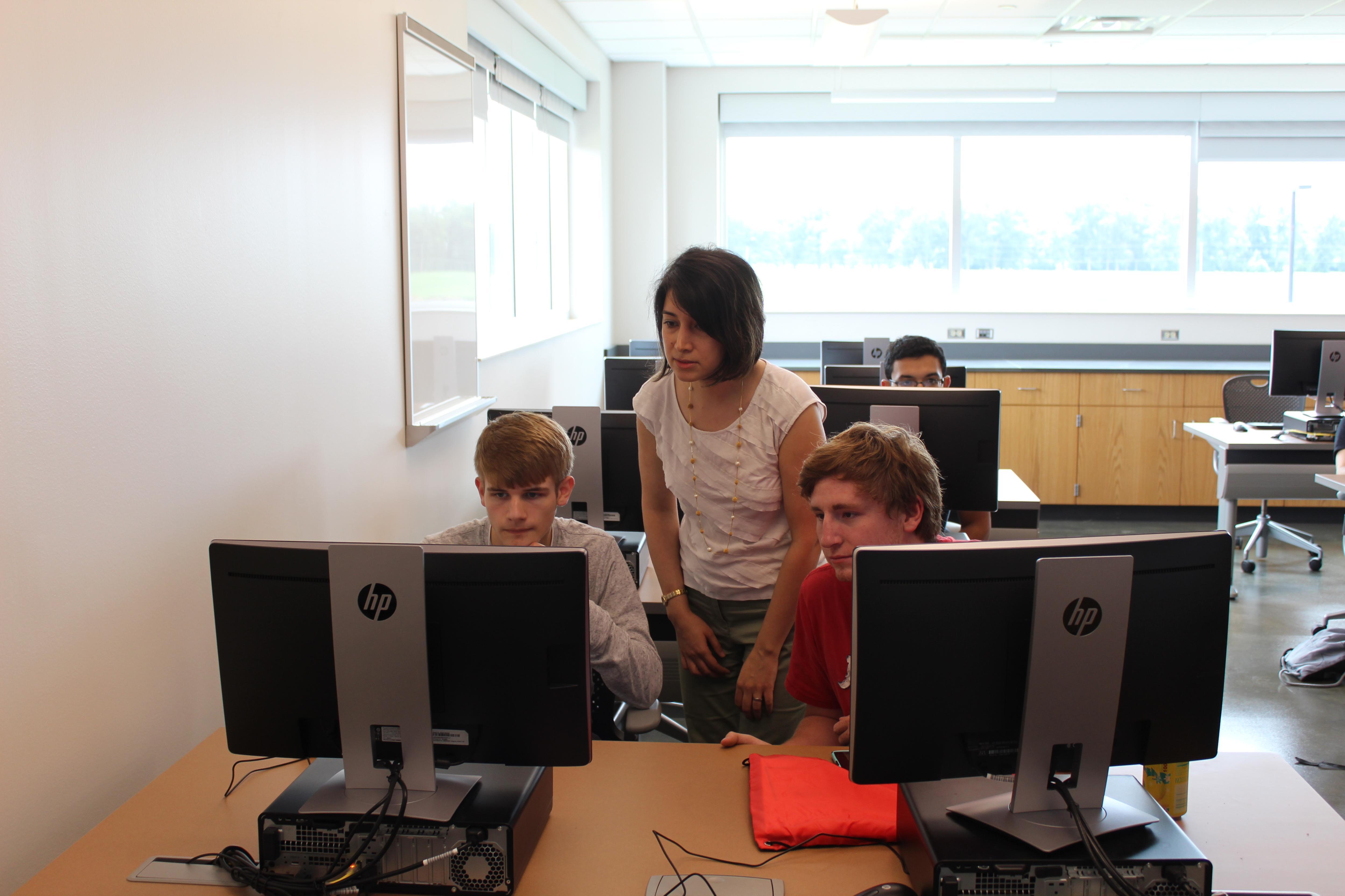 Woman assisting two male students in computer lab