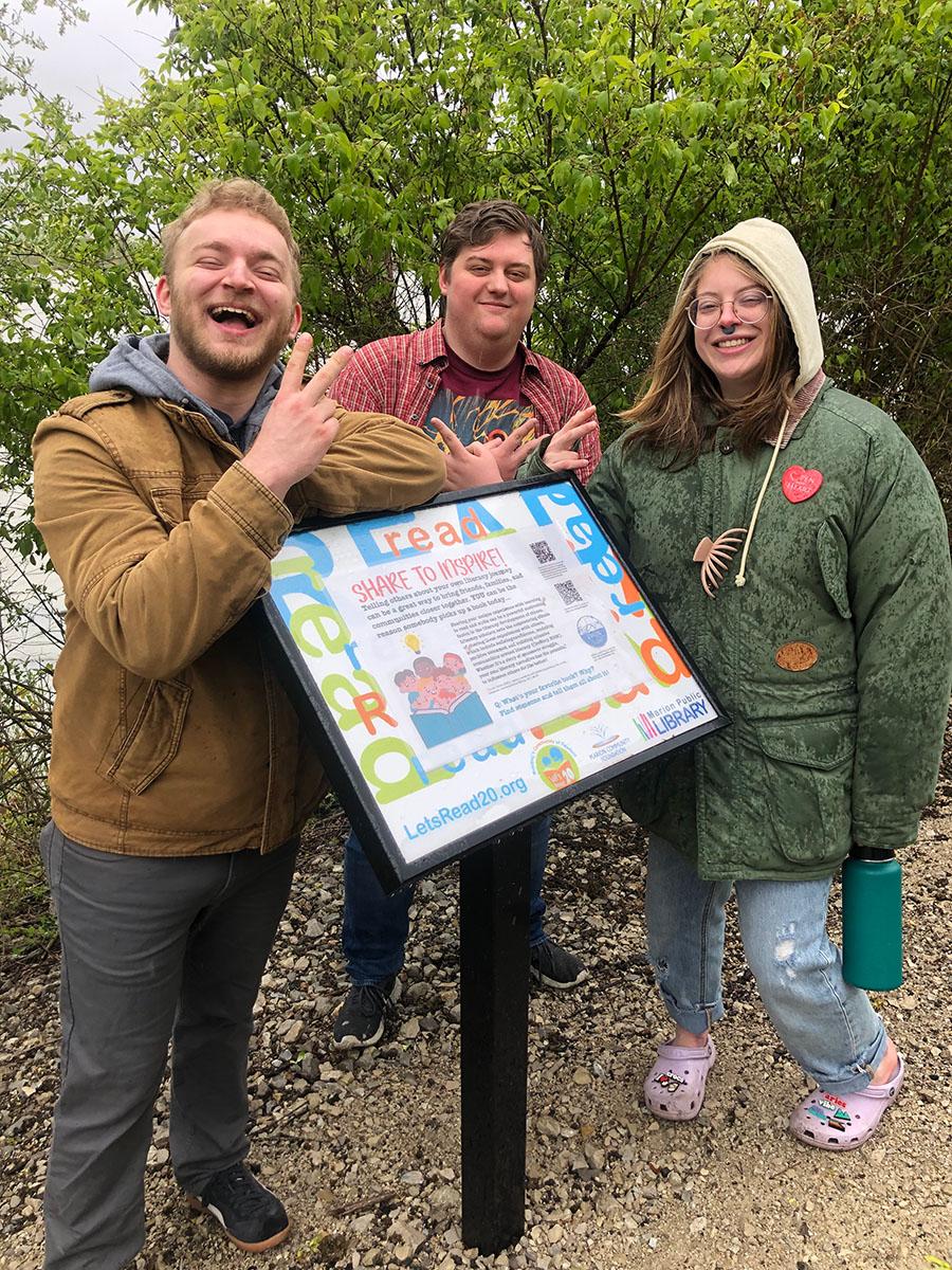 Three young people standing around a sign outdoors