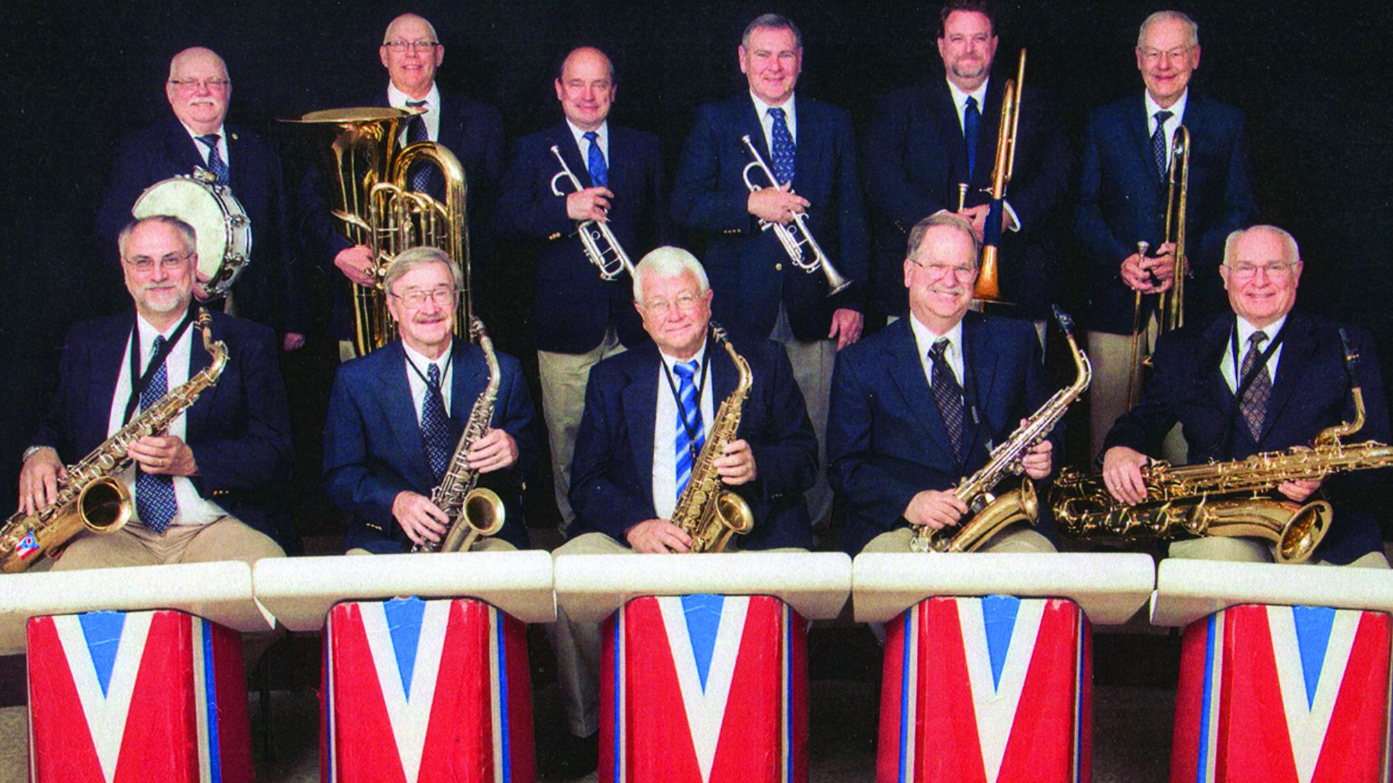 eleven member big band sitting with instruments in front of red, white, blue band stand