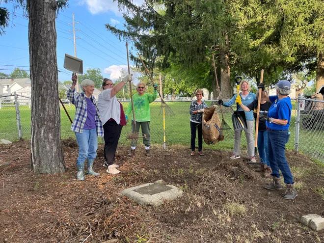 group of women in cemetery with gardening tools celebrating