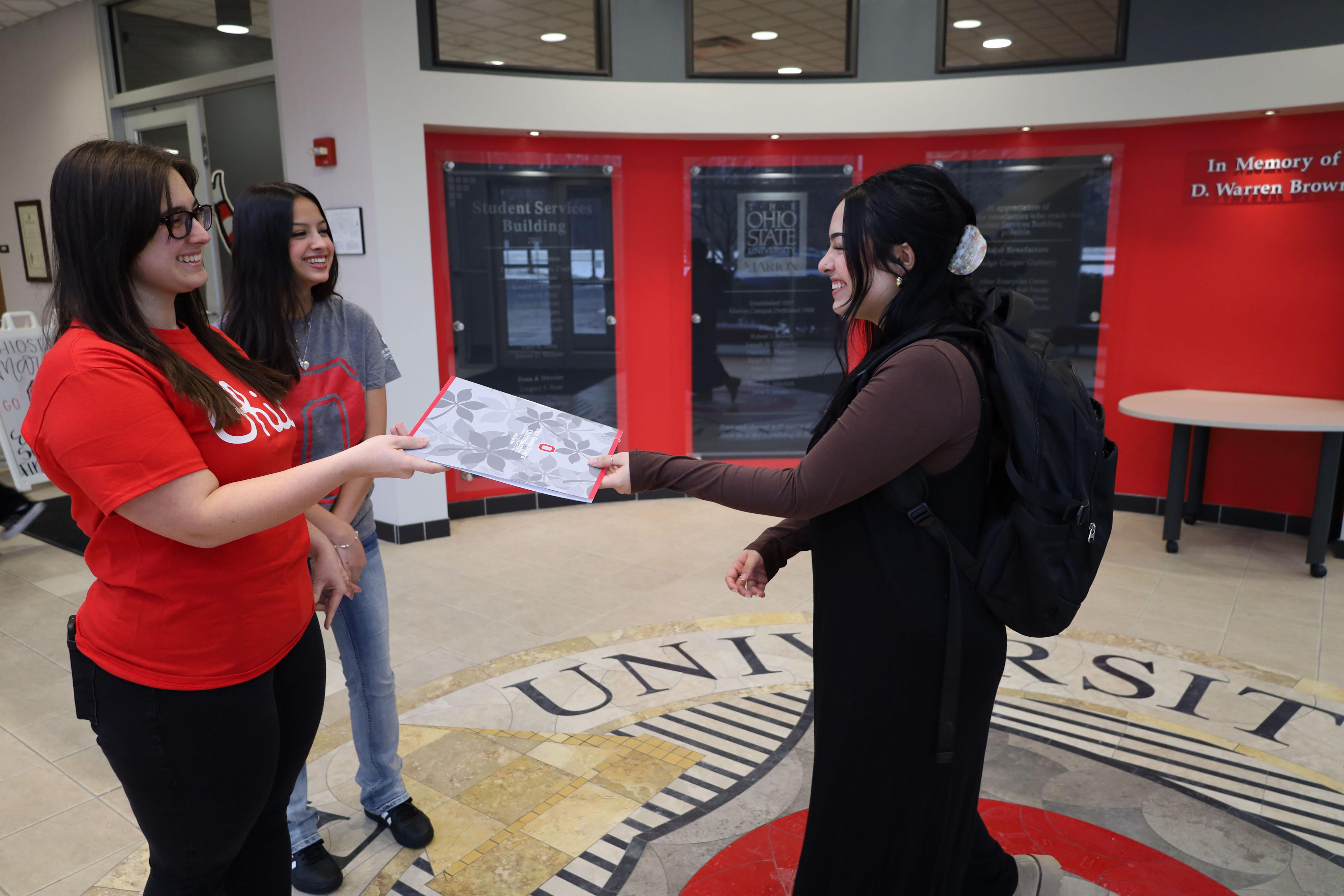 Two young ladies meet another and hand brochure