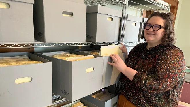 Woman in glasses looking through many file boxes