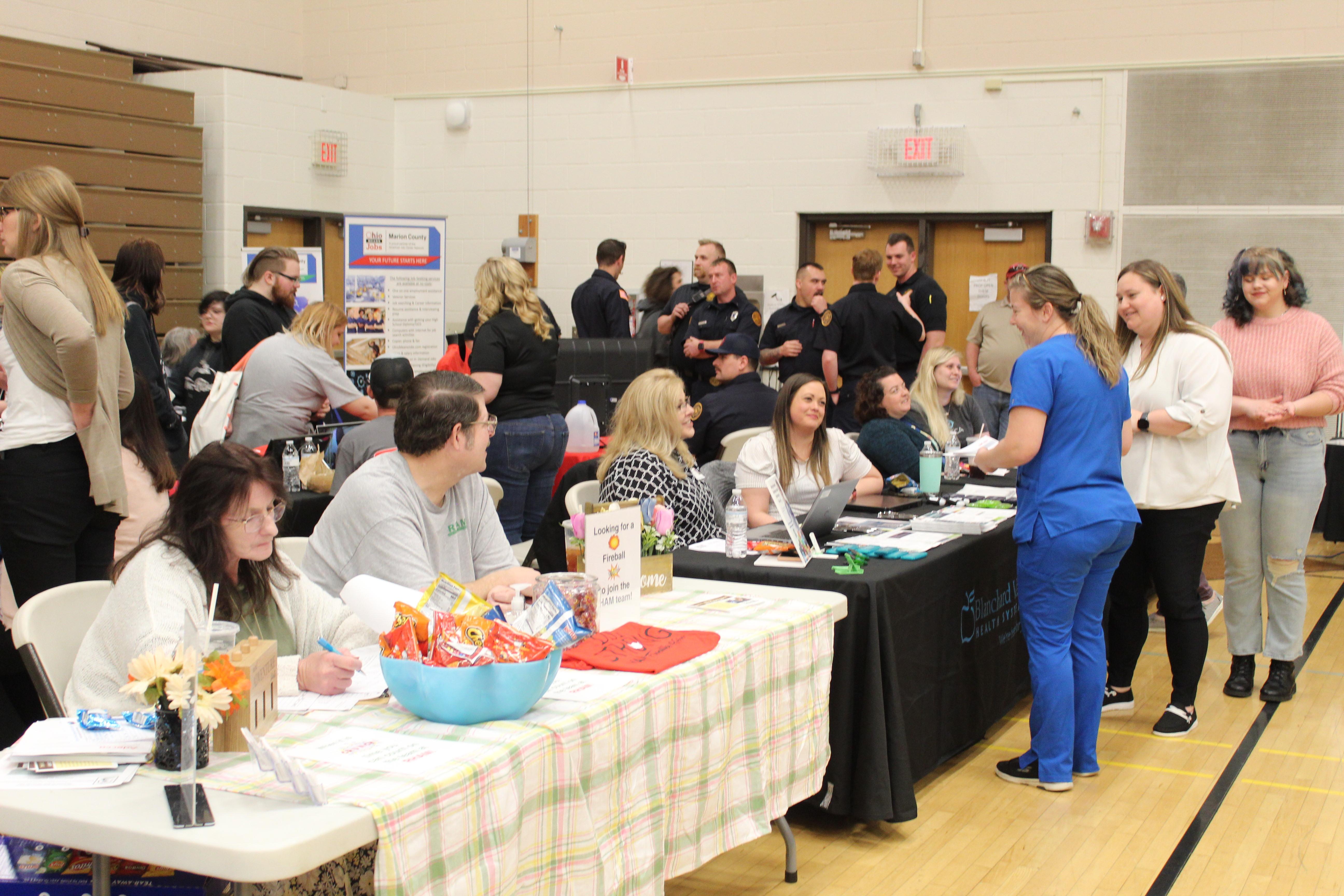 group of job seekers including nurse in blue scrubs at a table in gymnasium