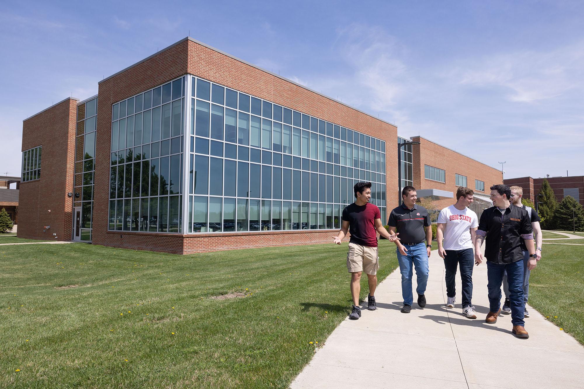 young men walk down sidewalk from large academic building