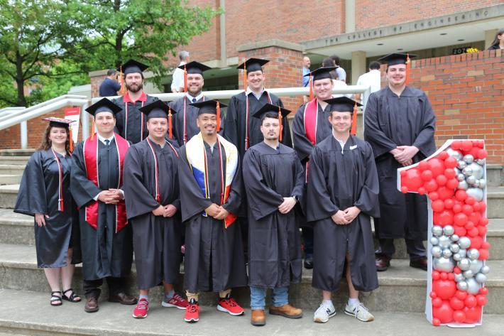 group of college graduates in cap and gown posed on steps