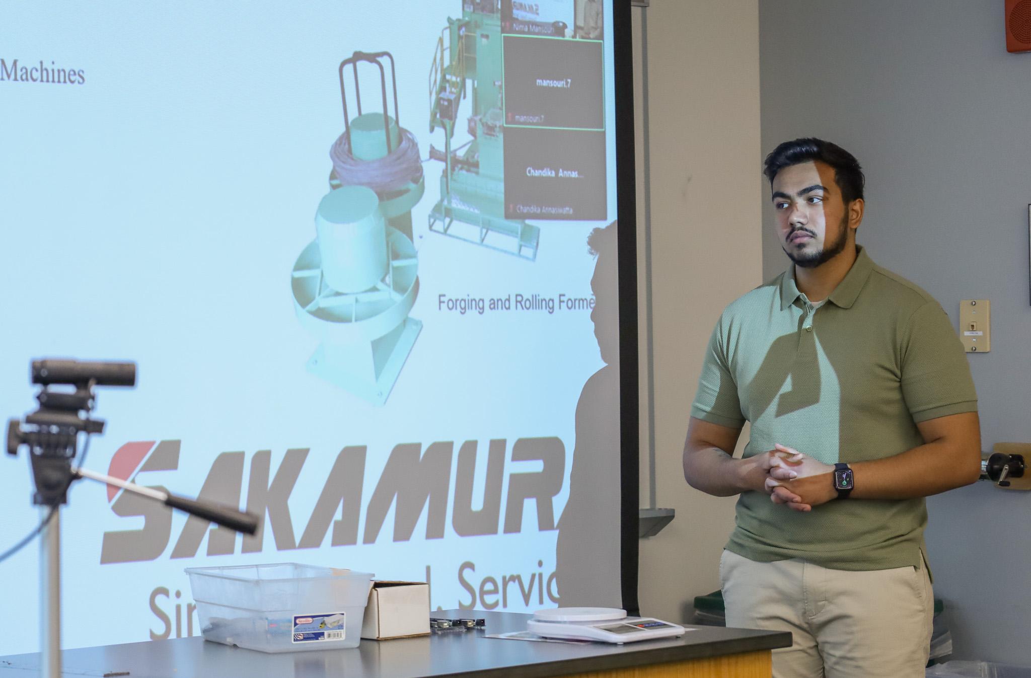 young man in green shirt presenting Power Point in a college classroom