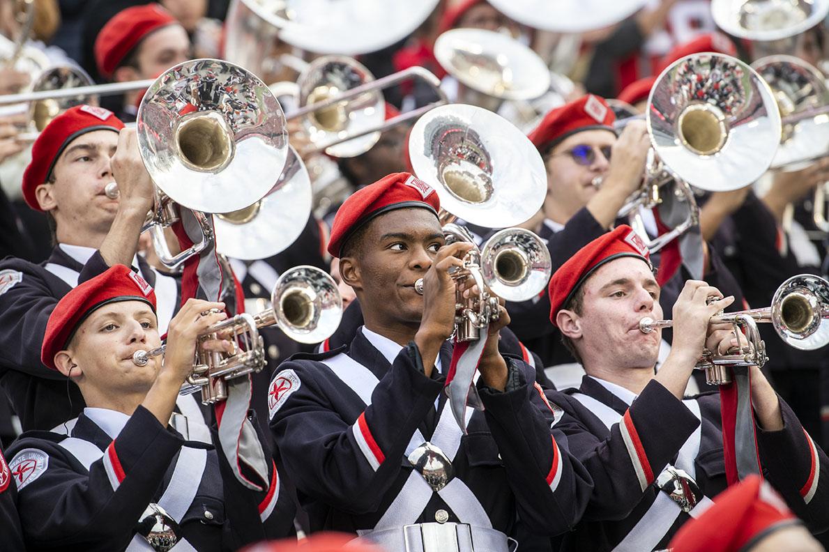 marching band group with silver brass instruments, black uniforms, and red beanies performing