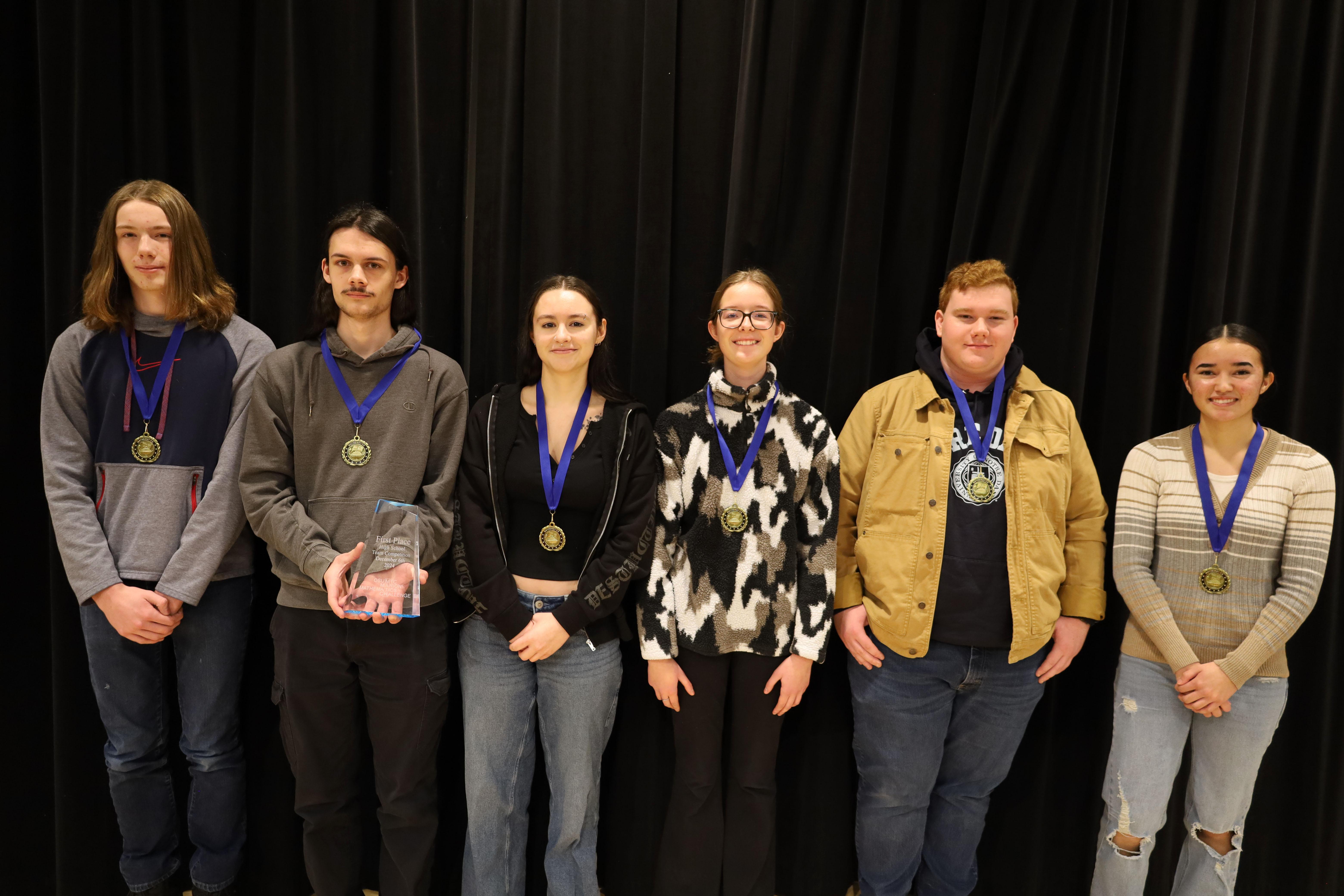 Six young people on stage wearing medals with blue ribbons