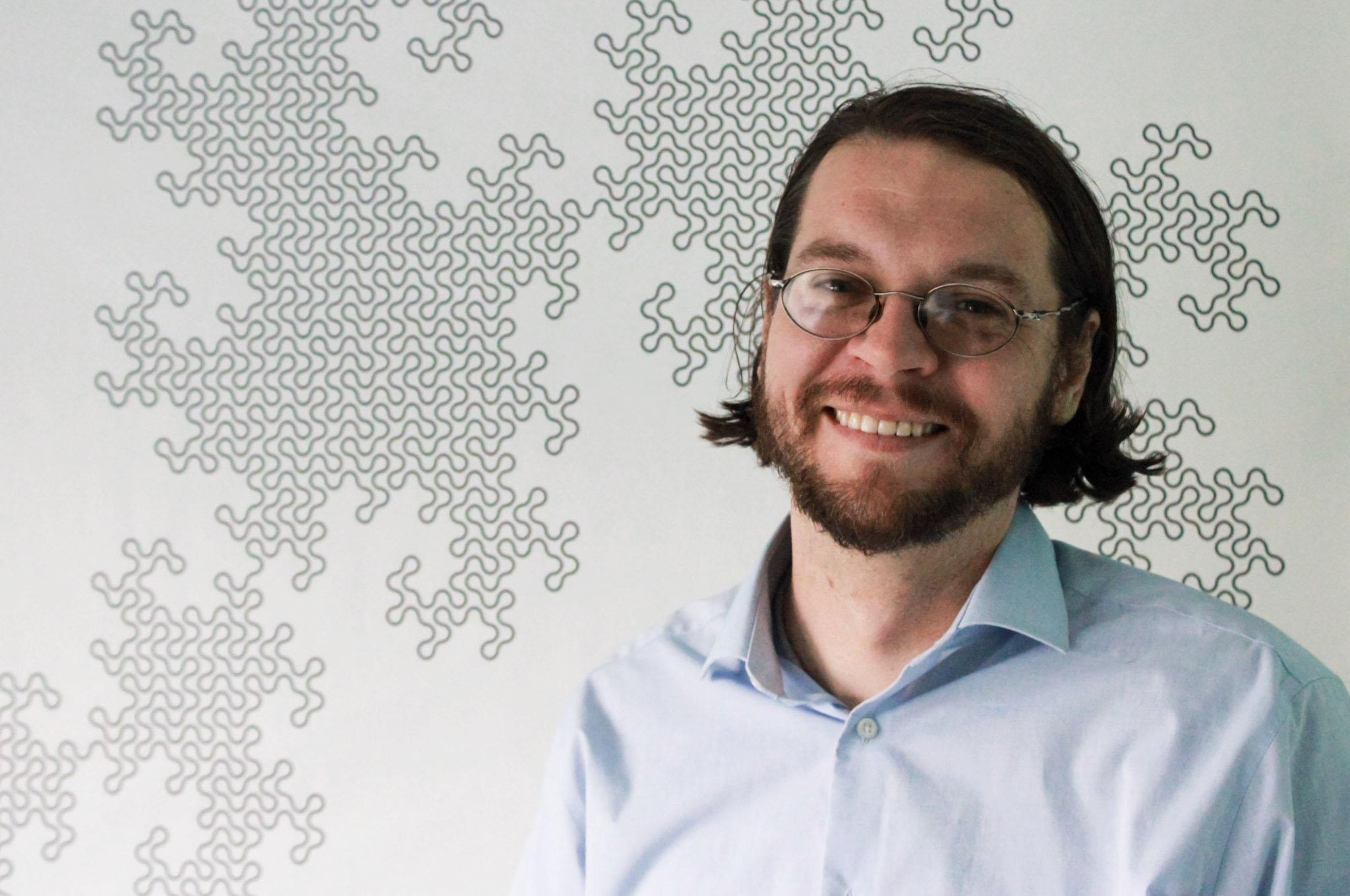 man in light blue shirt and glasses in front of fractal background